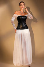 Woman wearing a black off-the-shoulder corset top with sheer white long sleeves and a long white sheer tulle skirt, standing with arms at her sides.