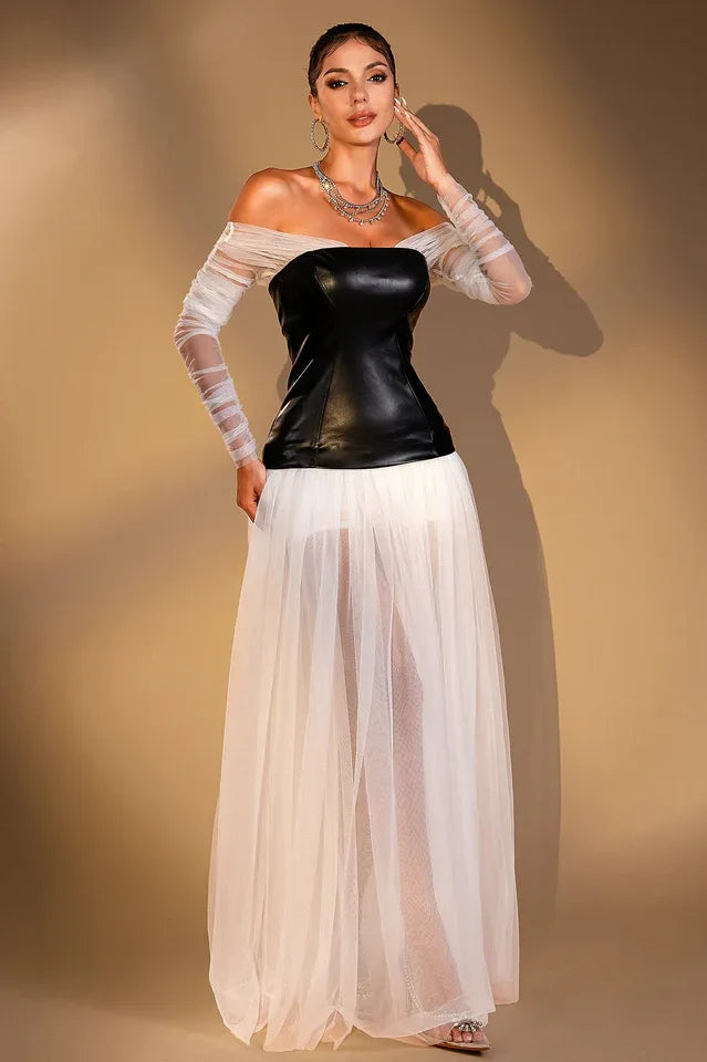 Woman wearing a black off-the-shoulder corset top with sheer white long sleeves and a long white sheer tulle skirt, standing with arms at her sides.