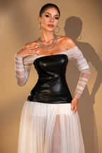 Close-up of a woman wearing a black off-the-shoulder corset top with sheer white long sleeves, layered necklaces, and hoop earrings.