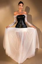 Woman wearing a black off-the-shoulder corset top with sheer white long sleeves and a long white sheer tulle skirt, holding the skirt out to the sides.