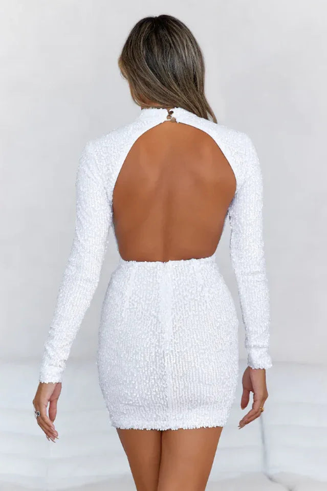 Back view of a woman wearing a white sequined long-sleeve mock neck mini dress with a backless design.