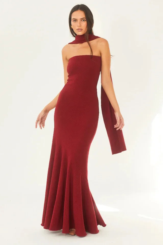 Woman wearing a red strapless mermaid gown with a scarf draped over one shoulder