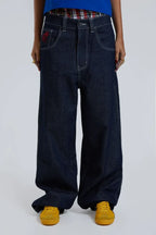 Close-up of woman's legs wearing dark wash wide leg jeans with plaid waistband detail and yellow shoes