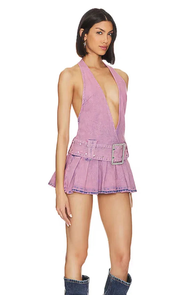 Woman wearing a lavender denim halter mini dress with a plunging neckline and pleated skirt, standing with a neutral expression.
