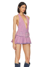 Woman wearing a lavender denim halter mini dress with a plunging neckline and pleated skirt, standing with a neutral expression.