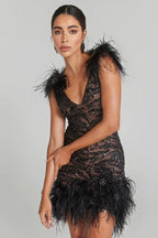 Woman wearing a black sequined mini dress with feather trim on the shoulders and hem, posing with arm bent.