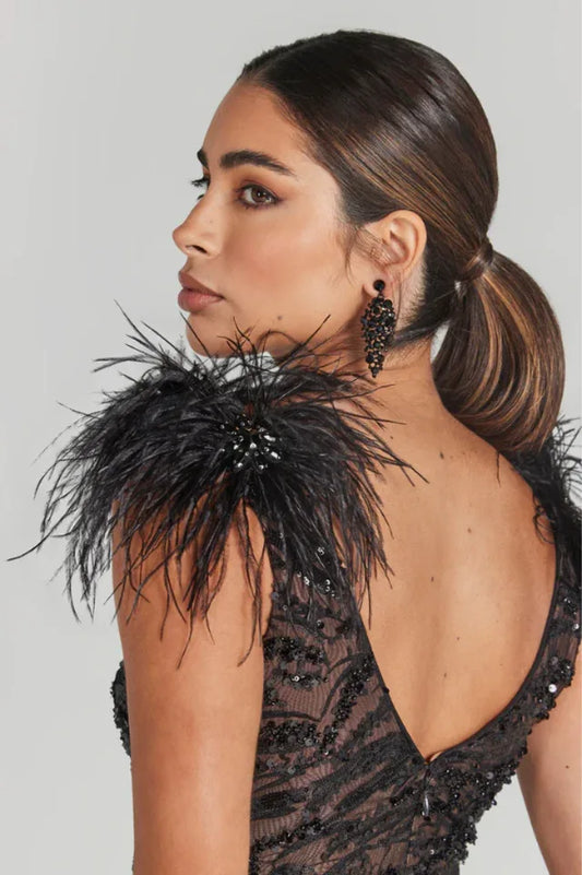 Close-up of the back of a woman's shoulder wearing a black sequined dress with feather trim and a black statement earring.