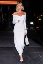 woman wearing a white off-the-shoulder ruched maxi dress and white handbag walking at night