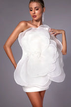Woman wearing a white one-shoulder mini dress with a large floral appliqué on the bodice, close-up.