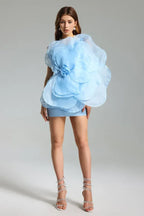Full-length view of a woman in a light blue one-shoulder mini dress with a large floral appliqué and jeweled heels.