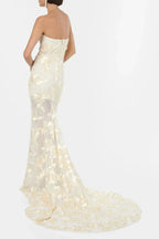 Back view of a woman in a strapless ivory gown with gold floral embroidery and a train.