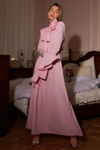 Woman posing in a pink maxi dress with a bow neck and flared sleeves, showcasing the draped fabric.
