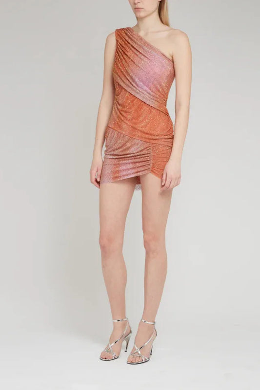 Full-length studio shot of a model wearing a shimmering one-shoulder mini dress with asymmetrical ruching and embellishments, paired with strappy silver heels.