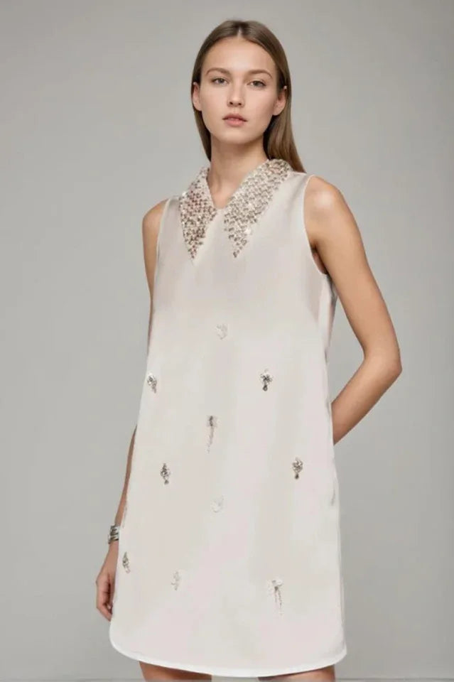 Model wearing a sleeveless ivory A-line mini dress with a heavily embellished pointed collar and scattered embellishments on the skirt.