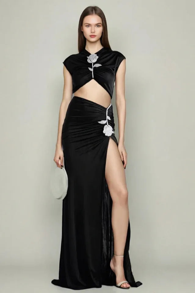 Woman in a black velvet evening gown with a cut-out detail, high slit, and embellished rose. Main image