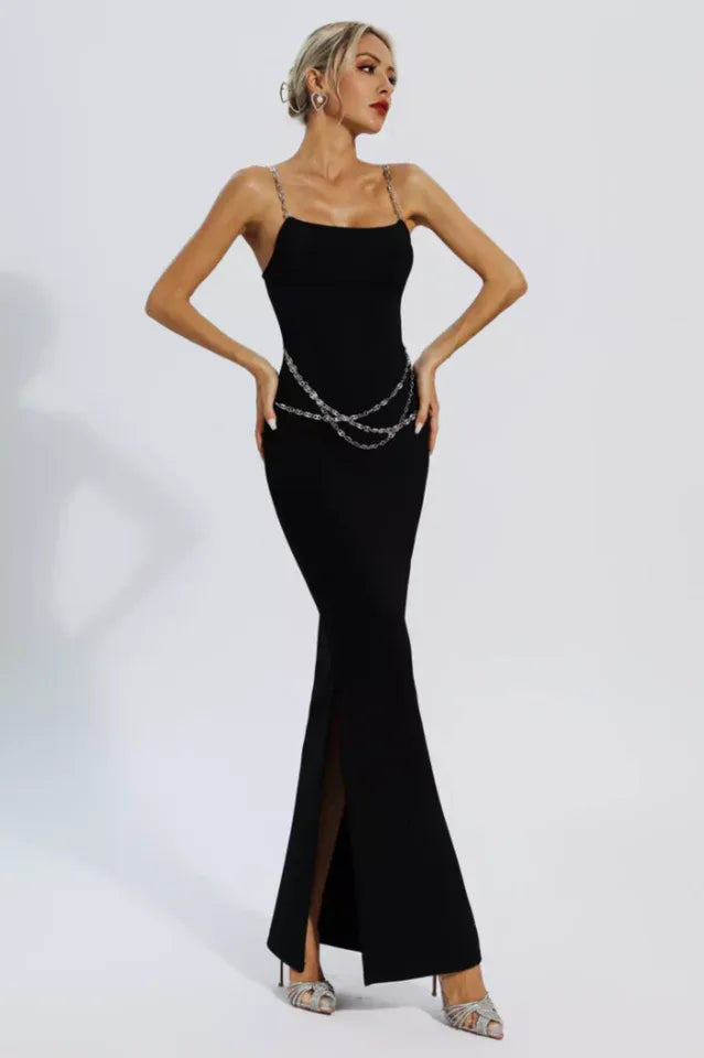 Woman wearing a black sleeveless maxi dress with chain straps and a chain belt, standing with hands on hips.