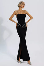 Woman wearing a black sleeveless maxi dress with chain straps and a chain belt, standing with hands on hips.