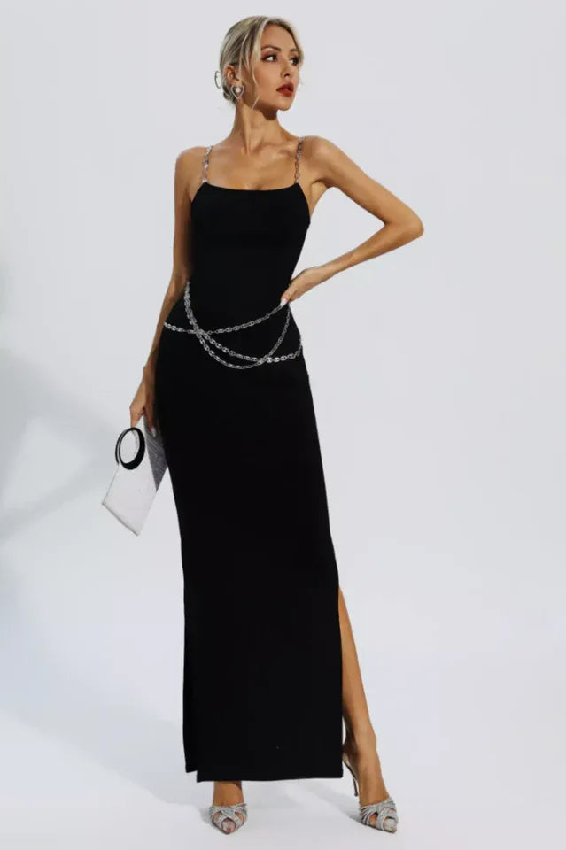 Woman wearing a black sleeveless maxi dress with chain straps and a chain belt, holding a clutch.