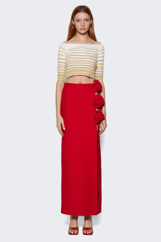 model wearing a red floor-length skirt with a high slit and rose embellishments on the side, paired with a striped crop top Main image