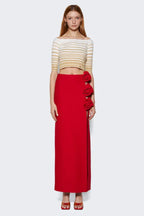 model wearing a red floor-length skirt with a high slit and rose embellishments on the side, paired with a striped crop top