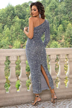 Back view of a woman in a grey sequined one-shoulder long-sleeve dress with a side slit.