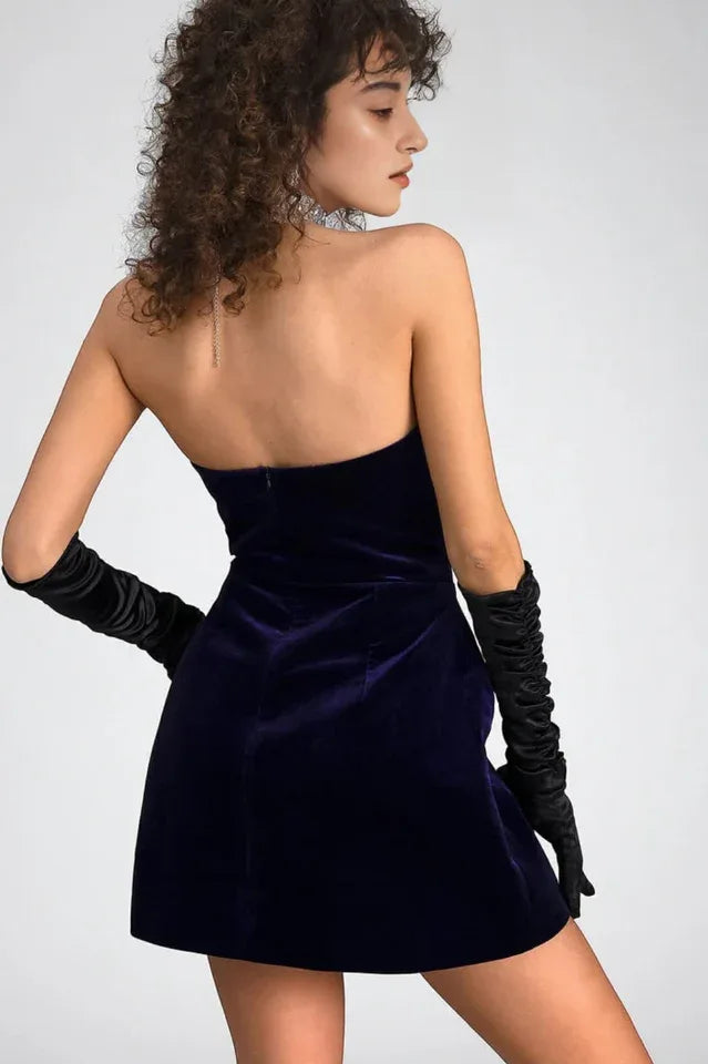 Rear view of the model in the purple velvet dress, highlighting the strapless back and mini skirt.