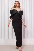 Full-length view of a woman in a black formal gown with a dramatic bow and sparkling accents