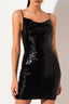 Woman wearing a black sequined mini dress with spaghetti straps and a cowl neckline, front view.