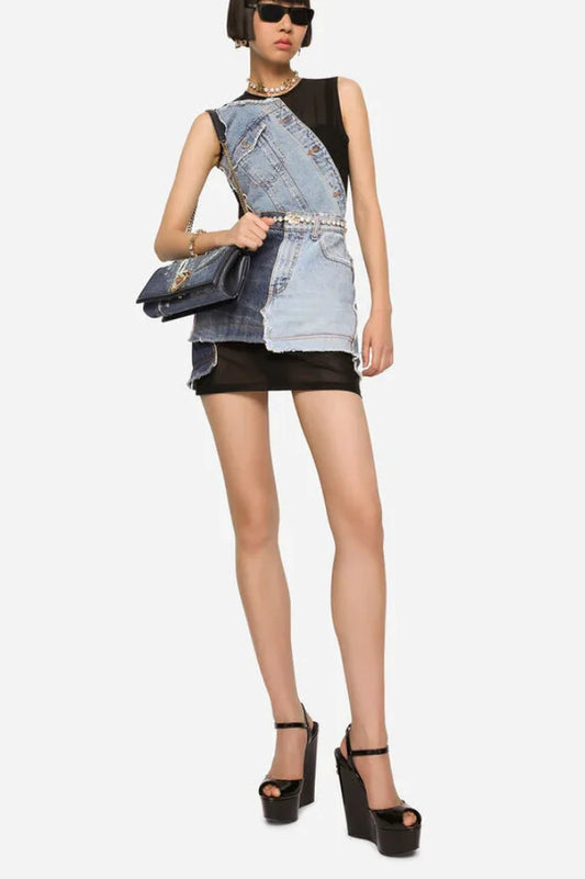 Full body shot of a model in a sleeveless black mesh mini dress with an asymmetrical deconstructed denim overlay, accessorized with a handbag and platform heels