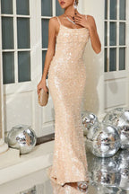 Woman holding a clutch and wearing a sequined mermaid dress with a cowl neckline and thin straps.