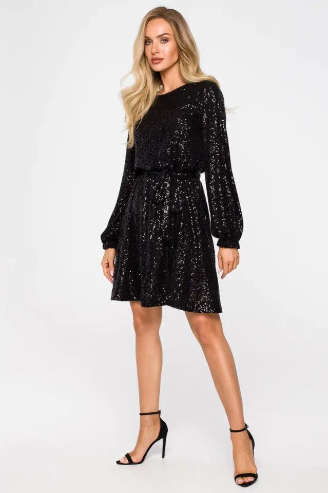 Woman wearing a black sequined A-line dress with long sleeves and a round neckline, cinched at the waist, paired with black strappy heels.