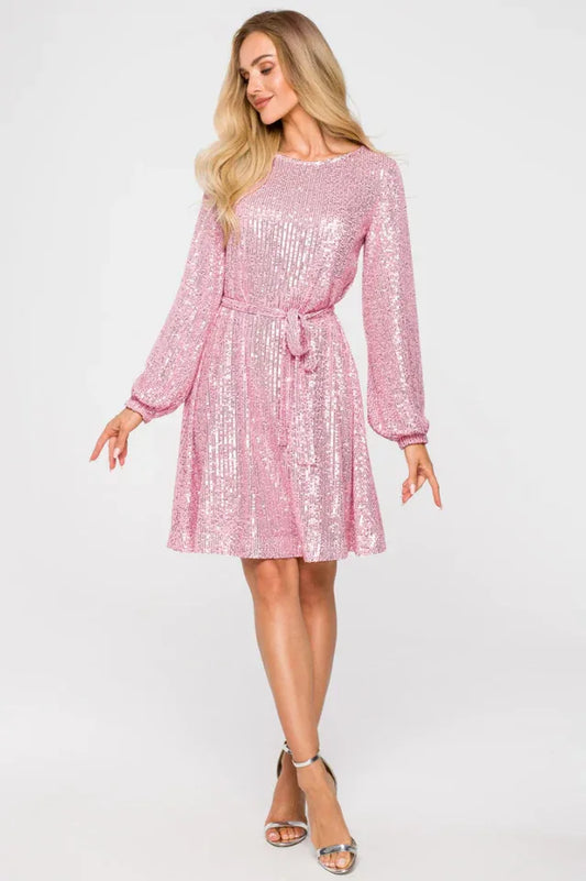 Woman wearing a pink sequined A-line dress with long sleeves and a round neckline, cinched at the waist with a matching belt, paired with silver strappy heels.