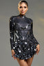 Woman wearing a black long-sleeve mini dress with mirror-like embellishments and a high neckline.