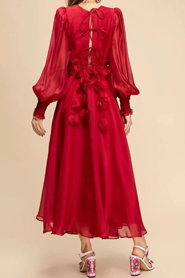 Back view of a woman wearing a long red chiffon dress with floral appliqués and bishop sleeves