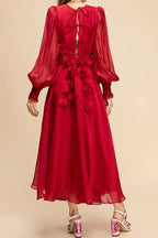 Back view of a woman wearing a long red chiffon dress with floral appliqués and bishop sleeves