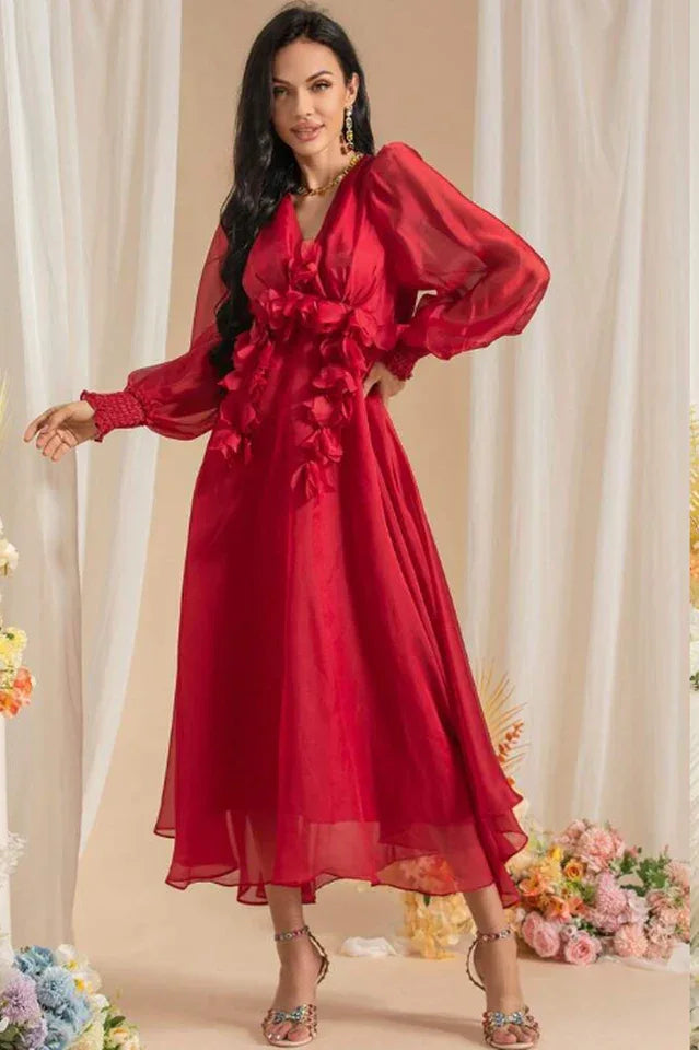 Woman posing in a long red chiffon dress with floral appliqués and bishop sleeves
