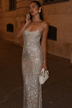 woman in a sequined silver gown with sheer straps, talking on the phone outdoors