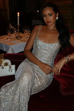 woman in a floor-length sparkling silver dress with an open back, seated on a red sofa