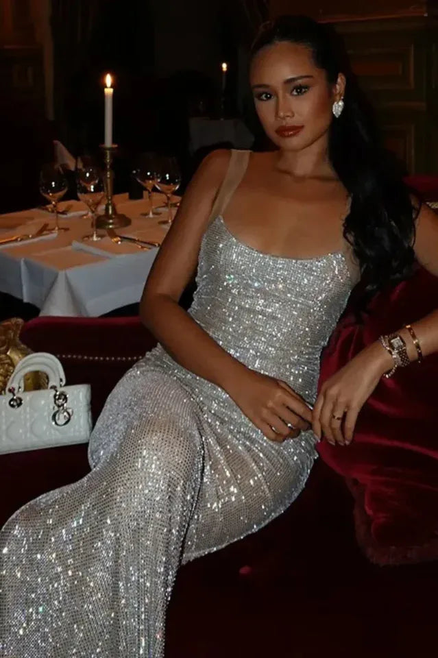 woman in a floor-length sparkling silver dress with an open back, seated on a red sofa