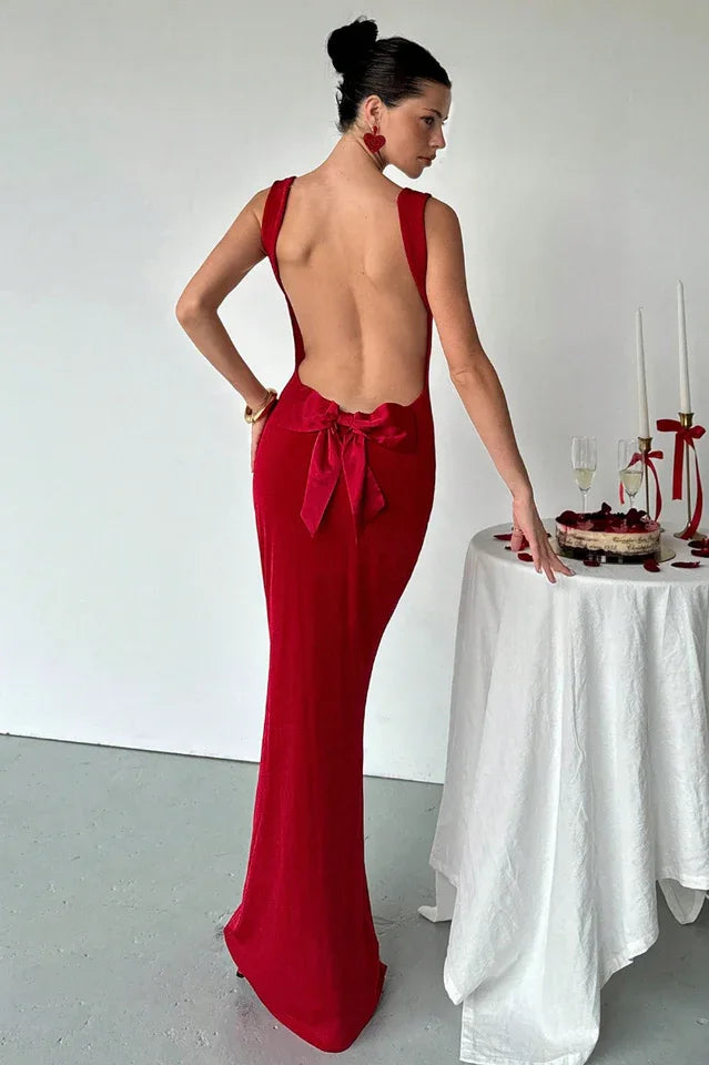 Woman wearing a long red velvet dress with a low back and a large bow detail.