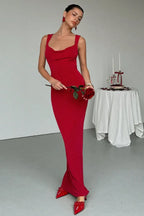 Woman wearing a long red dress with a cowl neckline and holding a red rose.