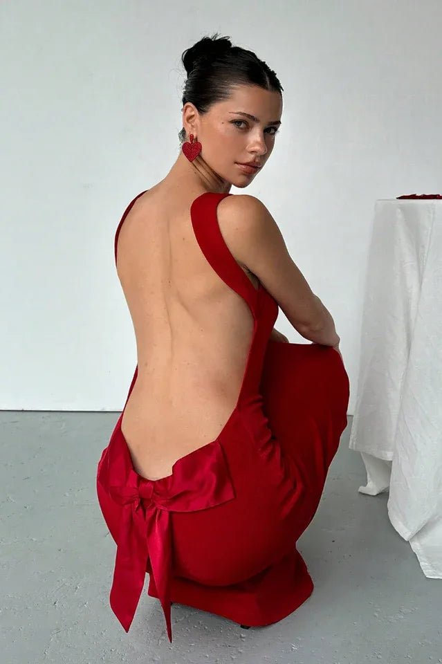 Woman wearing a red dress with a deep open back, showing a large satin bow.