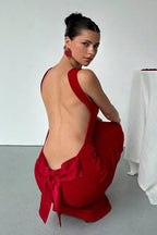 Woman wearing a red dress with a deep open back, showing a large satin bow.