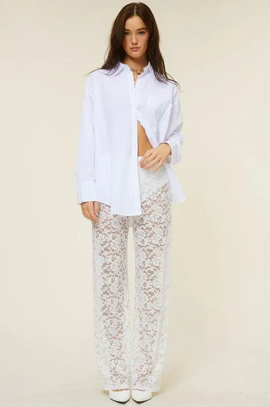 Woman wearing a white oversized button-down shirt unbuttoned to reveal midriff, paired with white lace wide-leg pants.