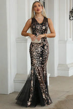 Woman in a black and gold sequined mermaid gown holding a gold clutch.