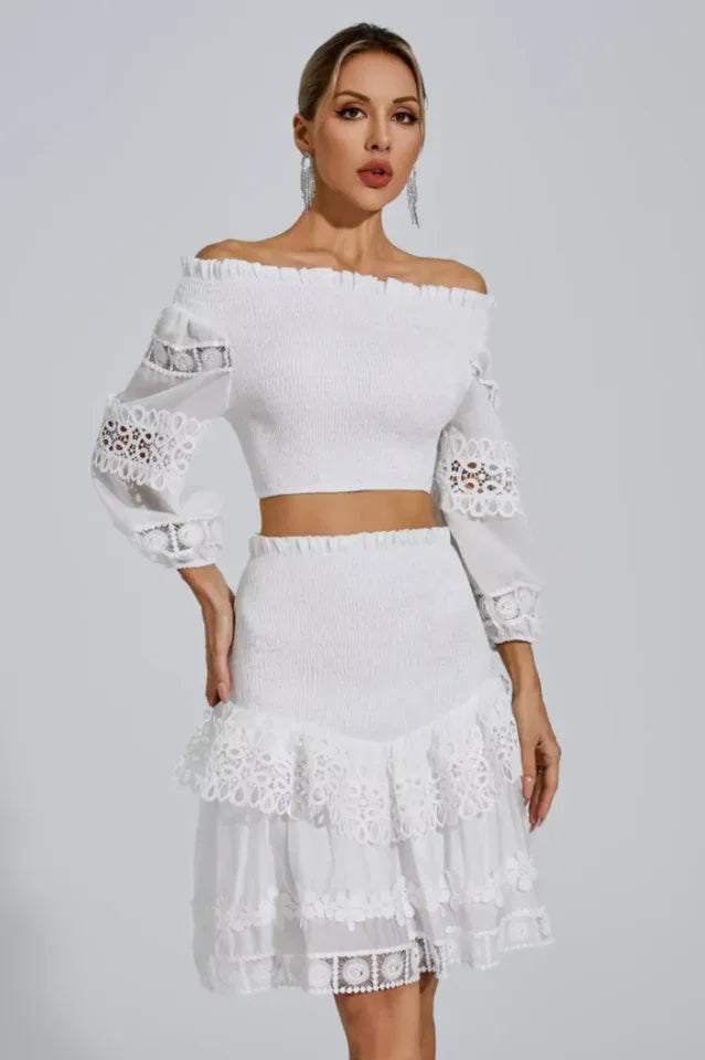 Woman wearing a white off-the-shoulder smocked crop top and a white tiered lace skirt Main image
