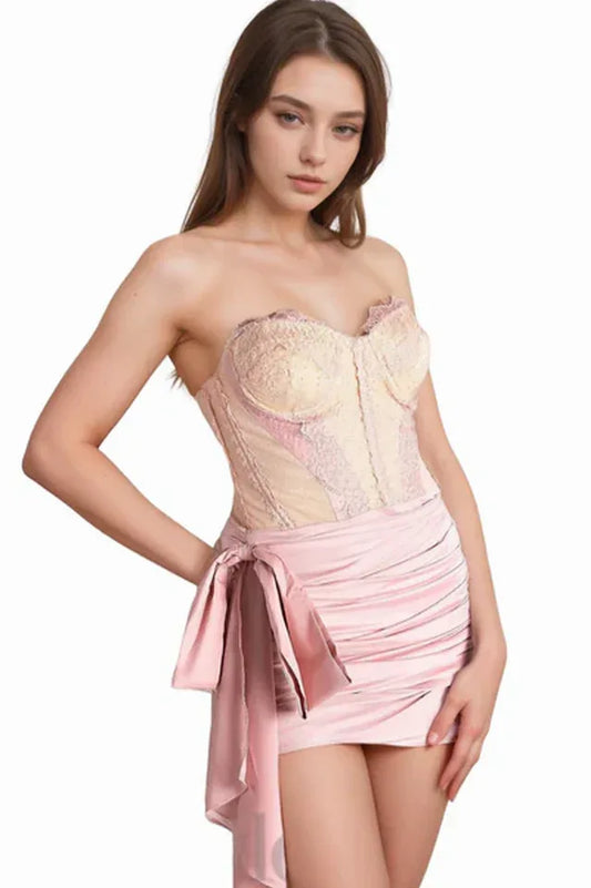 Woman wearing a pink strapless corset dress with a ruched skirt and bow detail.
