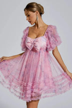 Woman wearing a pink floral print tulle dress with puff sleeves and a large bow detail on the bust.