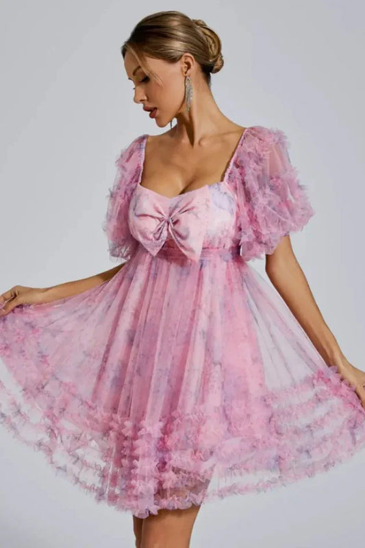 Woman wearing a pink floral print tulle dress with puff sleeves and a large bow detail on the bust.