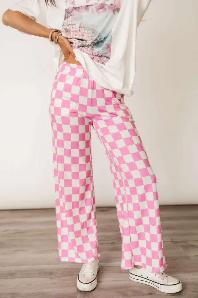 Woman's hands on hips wearing pink and white checkerboard wide leg pants and a graphic t-shirt.